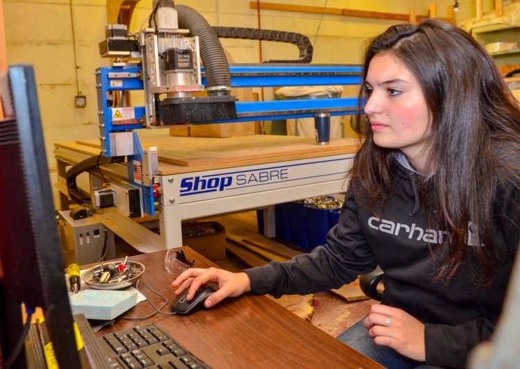 Sydney Birtwell sits at the computer that controls the CNC router behind her on Oct. 4 in the industrial arts wing of Maranacook Community High School. Birtwell set it up to cut many field hockey stick silhouettes on a sheet of plywood.