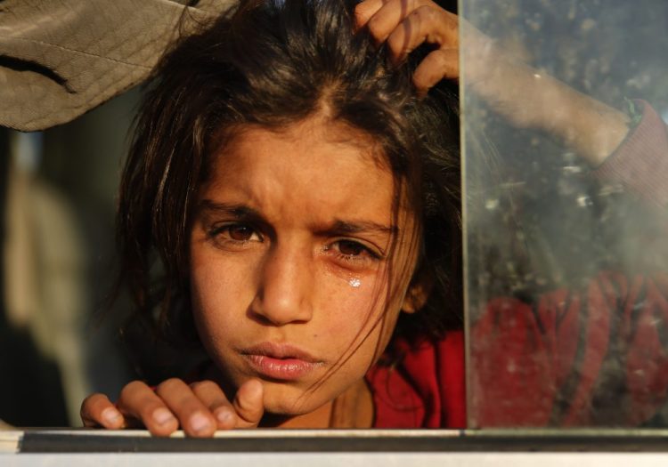 A Syrian girl who is newly displaced by the Turkish military operation in northeastern Syria weeps as she sits in a bus upon her arrival at the Bardarash camp, north of Mosul, Iraq, on Wednesday. The camp used to host Iraqis displaced from Mosul during the fight against the Islamic State group and was closed two years ago. The U.N. says about 160,000 Syrians have been displaced since the Turkish operation started last week, most of them internally in Syria. 