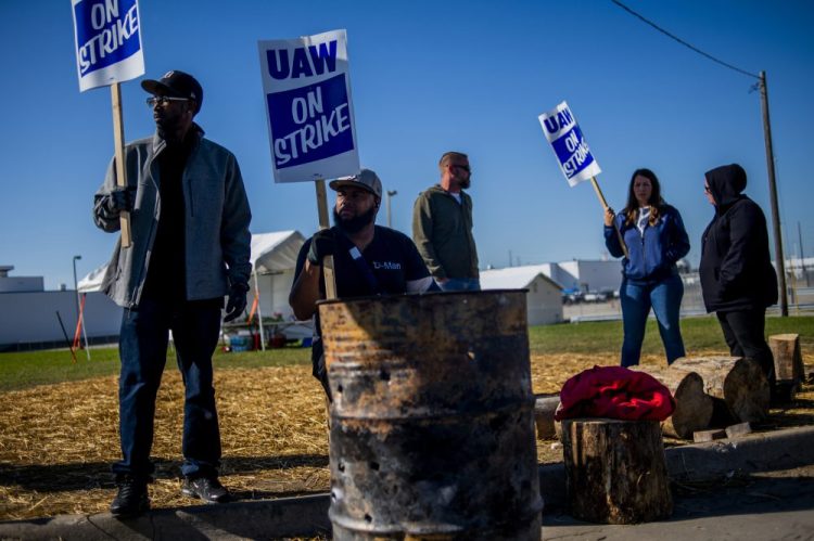 Detroit resident Jay Hawkins, left, and Flint resident Damien Moore picket outside of General Motors' Flint Paint Facility during the nationwide UAW strike against General Motors on Monday in Flint, Mich. An analysis estimates that as many as 100,000 workers – beyond the roughly 46,000 UAW strikers – have been laid off since the strike began. 