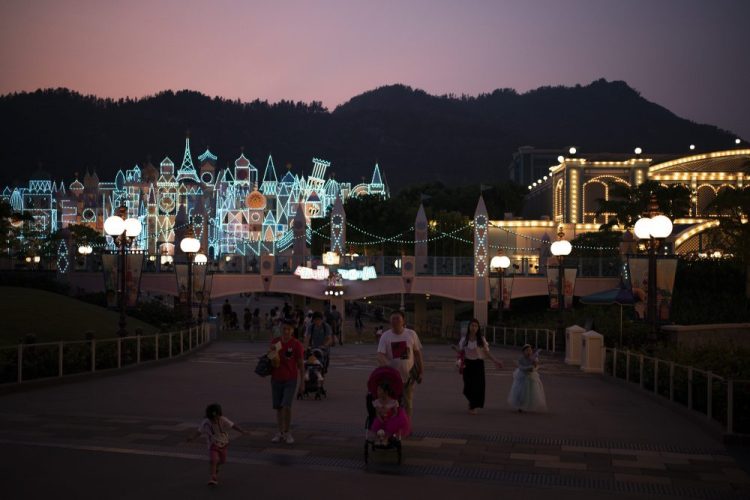 In this Oct. 11, 2019 photo, visitors walk at dusk in Hong Kong Disneyland in Hong Kong. 