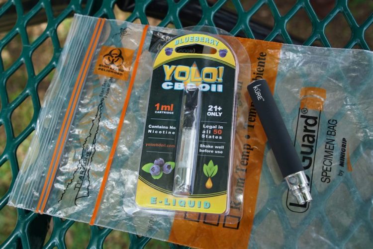 A Yolo! brand CBD oil vape cartridge sits alongside a vape pen on a biohazard bag on a table at a park in Ninety Six, S.C. More than 50 people around Salt Lake City had been poisoned by the time the outbreak ended early last year, most by a vape called Yolo!, the acronym for "you only live once." 