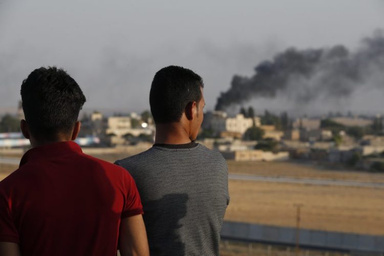 People standing on a rooftop in Akcakale, Sanliurfa province, southeastern Turkey, at the border with Syria, watch as smoke billows from fires caused by Turkish bombardment in Tal Abyad, Syria, on Sunday.
