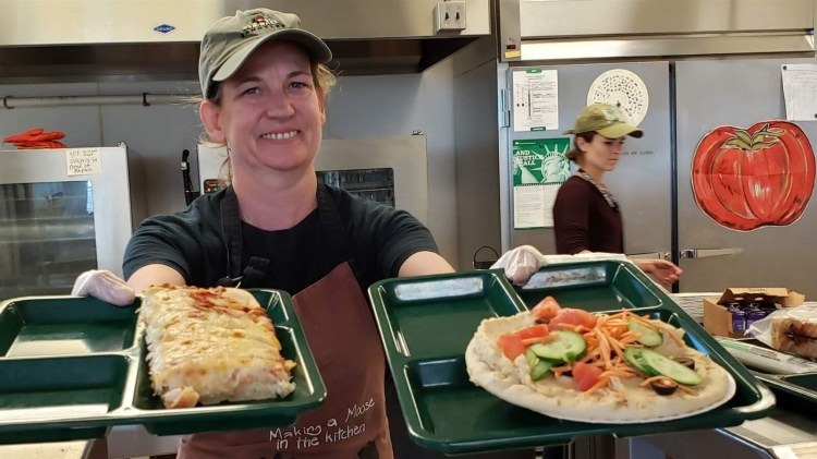 Portland school cafeteria worker Alison Mason shows off lunch options at East End Community School, including traditional pizza, left, and vegan pizza with hummus and vegetables. More schools are adopting vegan lunches, but a bill to allocate $3 million for plant-based lunch options is stalled in the California legislature.