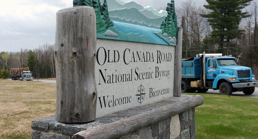 Staff photo by David Leaming
WELCOME: Loaded pulp trucks pass a large sign marking the site of a the Old Canada Road scenic byway property off US Route 201 in Solon. 