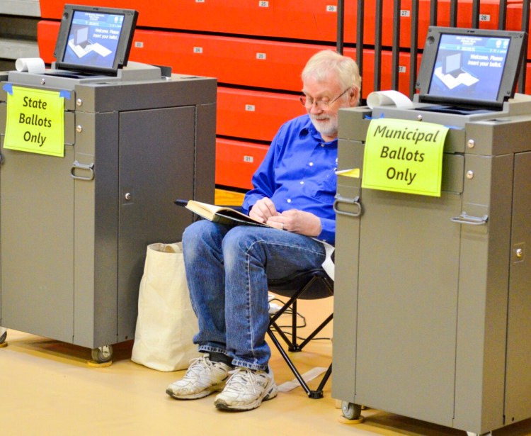 Flanked by voting machines, poll worker Harold Booth reads a book during a quiet moment Tuesday at Hall-Dale Elementary School in Hallowell.