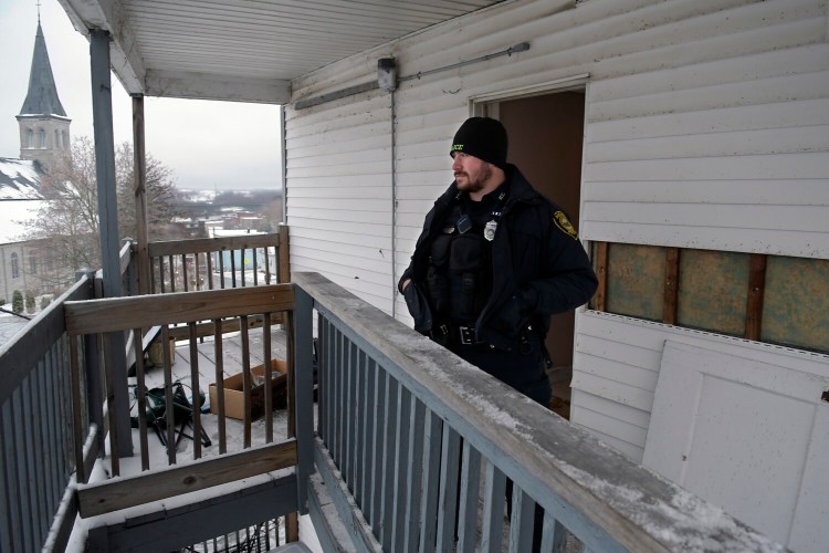 Augusta Police Officer Desmond Nutting stands  at the third floor entrance of 93 Northern Ave. in Augusta on Tuesday. Two bodies were recovered Monday in an apartment at the building. The structure is across the street from St. Michael Parish.