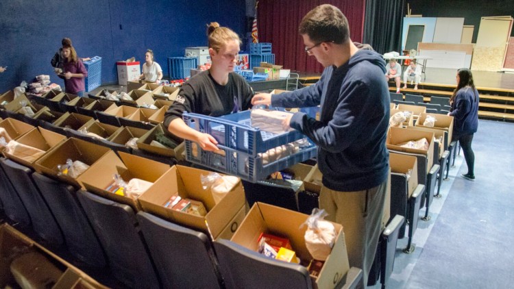 Hannah Foust, left, holds a bread rack as Jacob Lapierre packs a loaf into Thanksgiving baskets on Friday in the Little Theater at Gardiner Area High School.