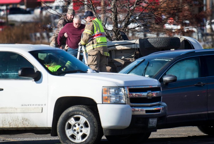 Waterville fire department rescue tech Shawn Stetson helps a man down from his overturned pickup truck Friday afternoon at the scene of a multi-vehicle crash at Elm Plaza and Main Street in Waterville. 