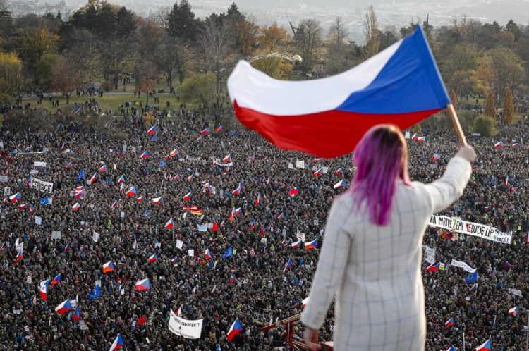 A woman waves a Czech flag from a roof as people take part in a large anti-government protest in Prague, Czech Republic, on Saturday. Czechs are rallying in big numbers to use the 30th anniversary of the pro-democratic Velvet Revolution and urge Prime Minister Andrej Babis to resign as peaceful protesters from all corners of the Czech Republic are attending the second massive protest opposing Babis. 