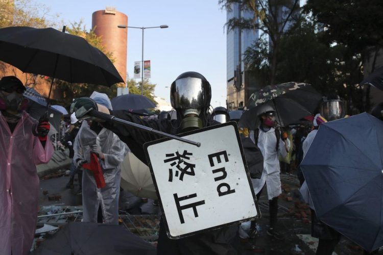 A protestor bangs a metal rod on a street sign Sunday during a confrontation at the Hong Kong Polytechnic University in Hong Kong. A Hong Kong police officer was hit in the leg by an arrow Sunday as authorities used tear gas and water cannons to try to drive back protesters occupying a university campus and surrounding streets.