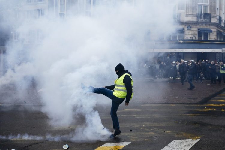 A protestor kicks away a tear gas canister during a yellow vest demonstration marking the first anniversary in Paris on Saturday. Police fired tear gas to push back yellow vest protesters trying to revive their movement on the first anniversary of the sometimes violent uprising against President Emmanuel Macron and government economic policies.