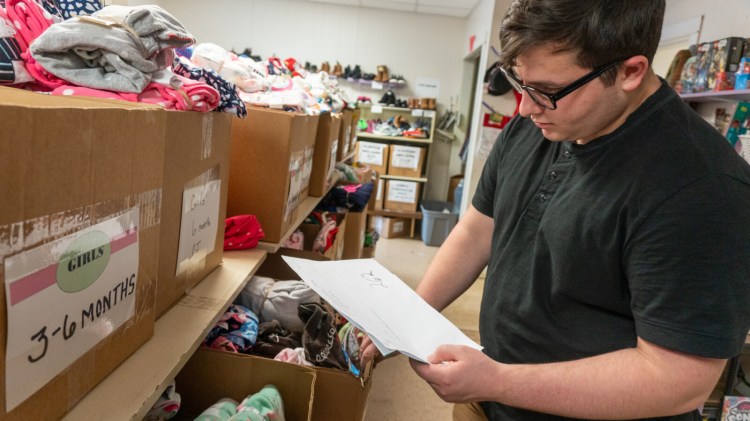 Keegan Drake, a volunteer at the Maine Children's Home for Little Wanderers in Waterville , is seen looking at items. This year donations are needed to fill the boxes for 1,700 children.