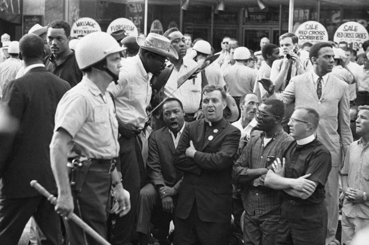 FILE - In this Aug. 6, 1966, file photo, Martin Luther King, Jr., kneeling on left, leads civil rights marchers in singing and praying in front of real estate office on Chicago Southwest Side. Neighborhoods that King visited included Chicago Lawn, where he was confronted by an angry white mob and was struck by a rock. "I have never seen, even in Mississippi and Alabama, mobs as hostile and as hate-filled as I've seen here in Chicago," King said at the time. (AP Photo/File)