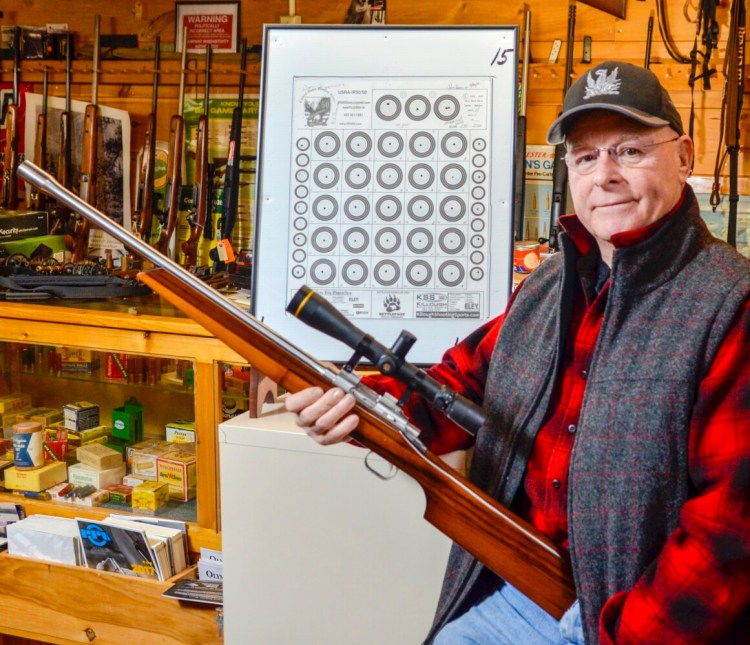 Gary Hamilton holds the Tony Larson .22-caliber sporter rifle Friday at Neilson's Sporting Goods in Farmingdale, the gun he used to shoot a 250-point 25X target next to him.