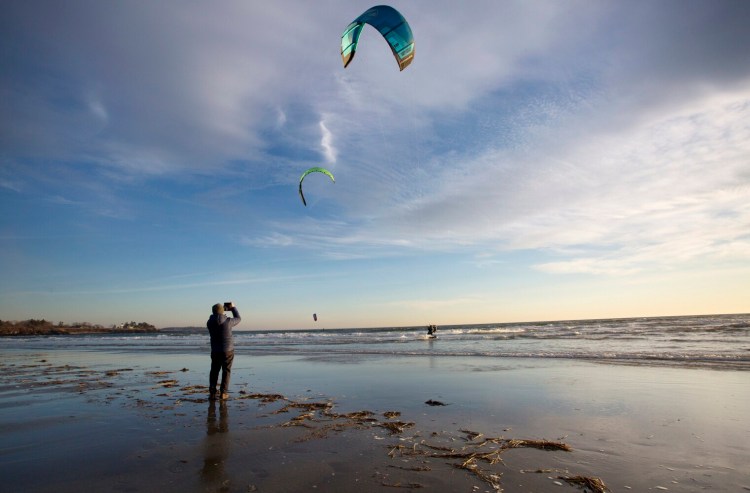 A beachgoer takes pictures of kitesurfers at Higgins Beach in December.