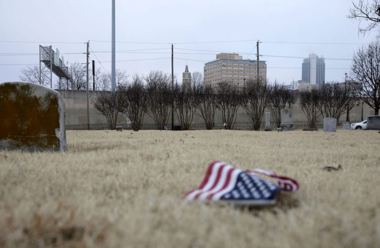 An American flag lies on the ground in front of an area of Oaklawn Cemetery. Tuesday, Dec. 17, 2019. in Tulsa, Okla.,  where a 25-by-30 foot apparent pit, consistent with a common grave, was located during initial scanning for unmarked graves related to the 1921 Tulsa Race Massacre. 