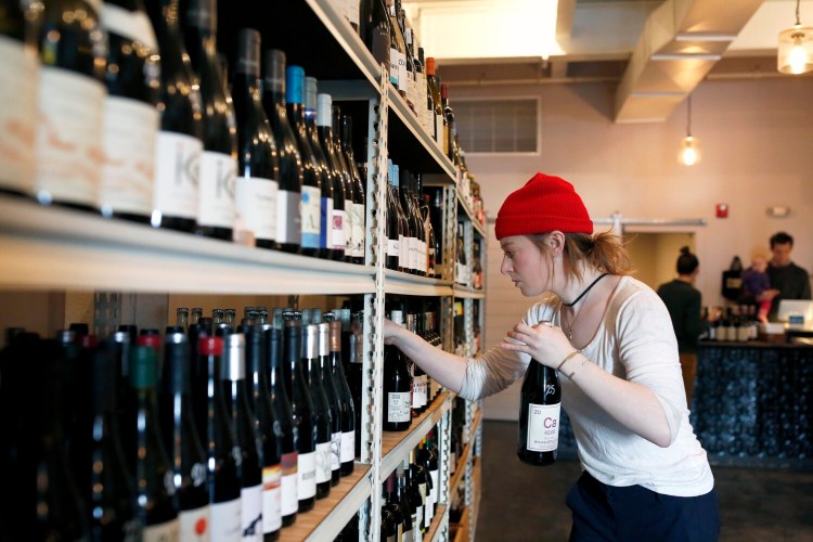 Lennie Newman stocks shelves at Maine & Loire wine shop on Tuesday. Severe tariffs on European wine, cheese and other products could devastate small businesses in Maine and across the U.S. 