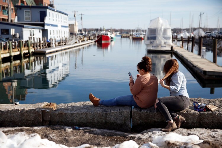 University of Southern Maine students Jordanna Ford, left, and Delaney O'Connor take in the sunshine on the Old Port waterfront next to Portland Pier in this February 2018 file photo. Portland is again looking for $24 million to remove silt from harbor wharves, and Maine lawmakers will back part of the project if federal money doesn't come through.