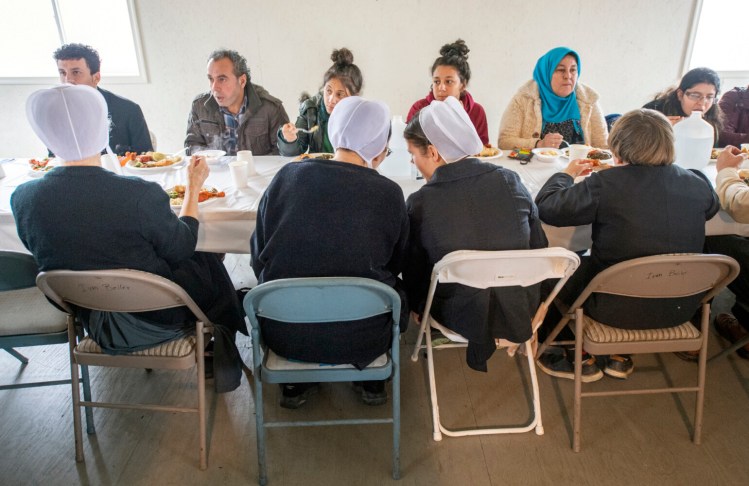 The Beiler family, in the foreground, eats with the refugees and visitors across from them. The event brings immigrants and neighbors together for a chance to share their stories and culture through food. (Paul Kuehnel/York Daily Record via AP)