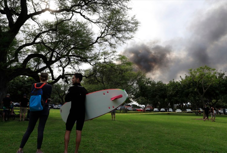 Kai Ohashi, right, and Lucy Taylor observe billowing smoke from a house fire after a shooting and domestic incident at a residence on Sunday in Honolulu. Witnesses say at least two police officers were shot and two civilians were injured. 