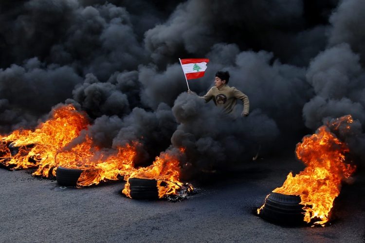 An anti-government demonstrator jumps on flaming tires to block a main highway during a protest in the town of Jal el-Dib, Lebanon, on Tuesday. Following a brief lull, Lebanese protesters returned to the streets in renewed rallies against a ruling elite they say has failed to address the economy's downward spiral.