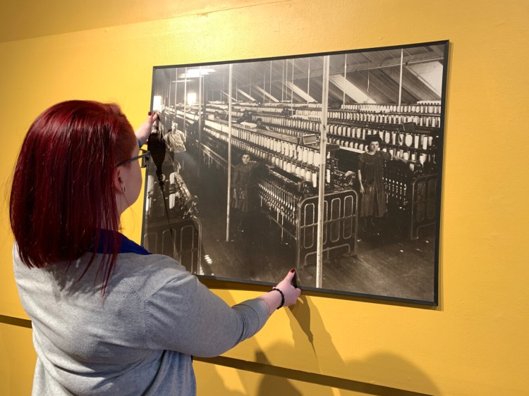 Emma Sieh, collections and exhibits coordinator at
Museum L-A, installs one of the reproduction photographs of children
working in the textile mills in the gallery for the upcoming child
labor exhibit "All Work and No Play" that opens January 30. The
reproduction is on loan from the USM Franco American Collection.
