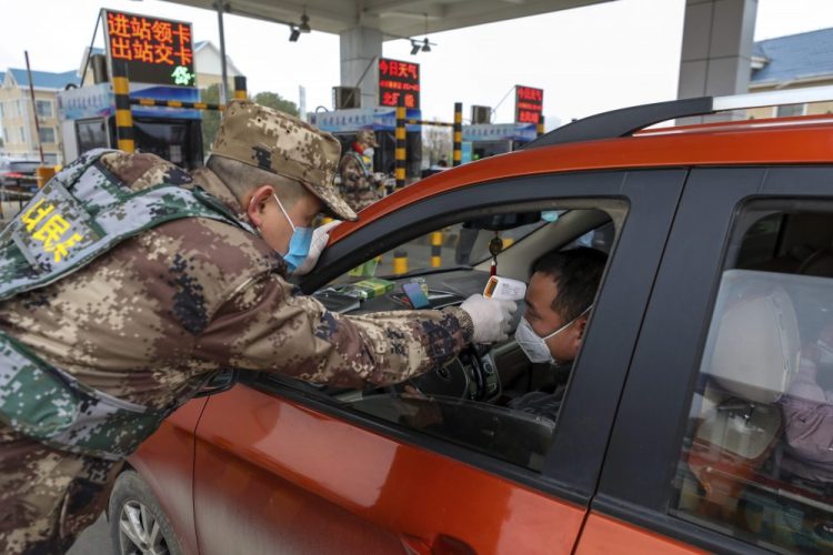 A militia member uses a digital thermometer to take a driver's temperature at a checkpoint at a highway toll gate in Wuhan in central China's Hubei Province, Thursday.
