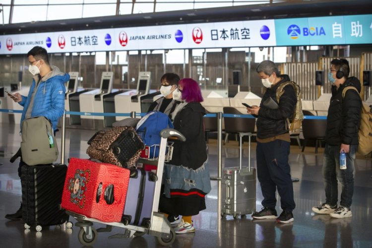 Travelers wearing face masks line up near the Japan Airlines check-in counters at Beijing Capital International Airport in Beijing, Thursday.