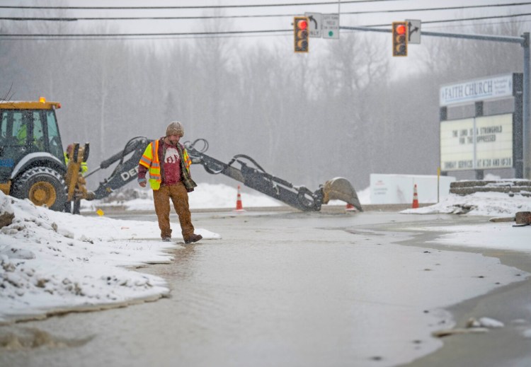 Justin Hort, a utility locator for USIC, stands next to a small river as crews work to repair a water main break Tuesday at the entrance of Shaw's Plaza on Kennedy Memorial Drive in Waterville.
