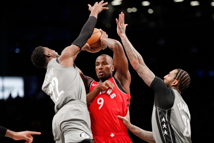Brooklyn's Caris LeVert, left, and Wilson Chandler defend Toronto's Serge Ibaka during Wednesday's game in New York. 