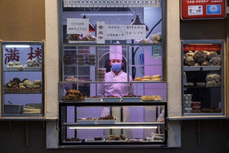 A chef looks out from behind a display of food products at a restaurant in Beijing, China. Regulators on Monday promised tax cuts and other aid to help companies recover from China's virus outbreak.