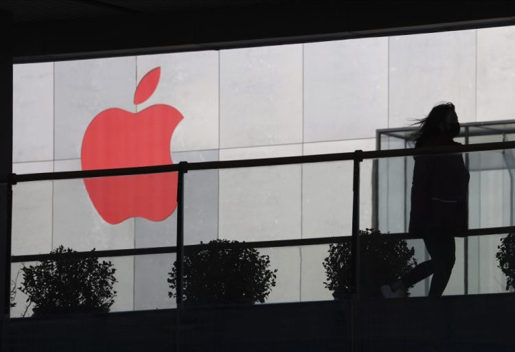 A woman runs past a Apple logo colored red in Beijing, China. Apple is temporarily closing its 42 stores in mainland China, one of its largest markets, as a new virus spreads rapidly and the death toll there rose to 259.