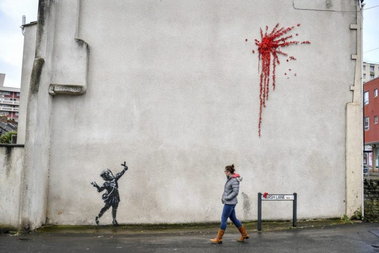 A woman walks past Banksy's newest mural  on the side of a house in Bristol, England, on Thursday. The art has since been covered after it was defaced. 