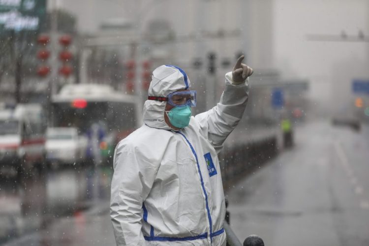 A worker wearing a protective suit gestures to a driver outside a hospital newly designated to treat COVID-19 patients in Wuhan, China, on Saturday. 