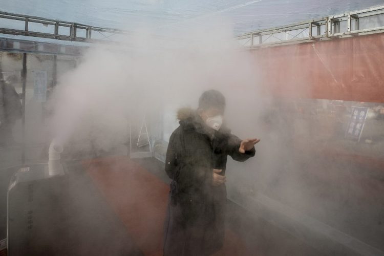 A man walks through a cloud of disinfectant spray to return home in China's Tianjin Municipality on Tuesday. There are no proven treatments or vaccines for the new coronavirus, officially named COVID-19.