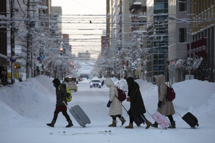 Tourists crosses an icy street with their luggage in Sapporo, Hokkaido, Japan, this month. The Japanese island of Hokkaido is declaring a state of emergency over the rapid spread of the new virus there. 