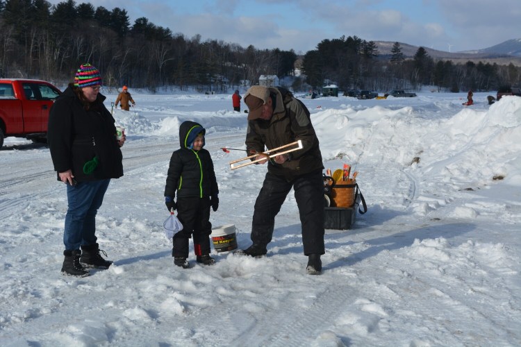 Alan Hart, right, shows Connor Metcalf, 6, of Phillips, how to set an ice fishing trap as Connor’s mother, Shannon Metcalf looks on.