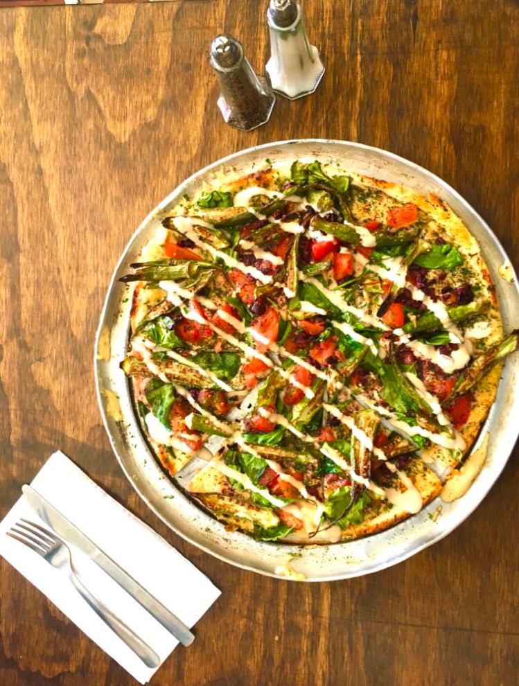 Pizza topped with hummus, fried okra, tapenade, tomatoes, spinach and tahini sauce is a regular special at Olive Cafe. If the feta cheese is omitted, the pizza is vegan.