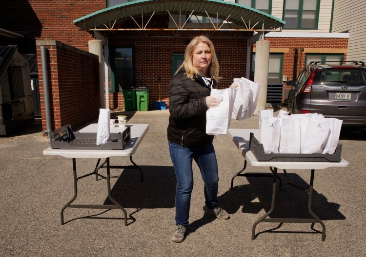 CUMBERLAND, ME - MARCH 16: Pam Stone, a bus driver for MSAD 51, carries bags containing breakfast and lunch to a family's car at the Mabel I. Wilson School in Cumberland on Monday, March 16, 2020. The district distributed breakfasts and lunches to 40 students on Monday. (Staff Photo by Gregory Rec/Staff Photographer)