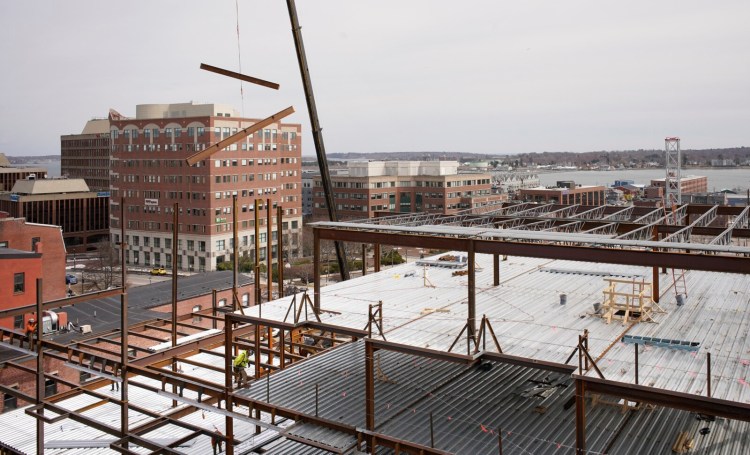 Iron beams are swung into place over a six-story apartment development on Free Street in Portland on Wednesday. For the most part, work is continuing on construction projects in Maine, although companies are taking precautions to protect workers from coronavirus exposure. 