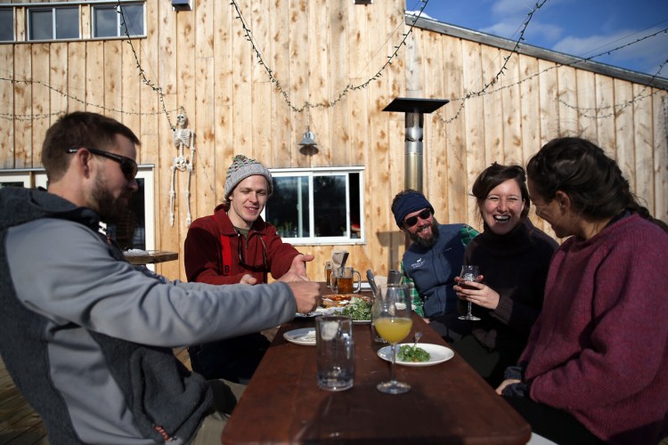 A group of friends enjoys beer and lunch on the back deck after cross-country skiing at Oxbow Beer Garden. 