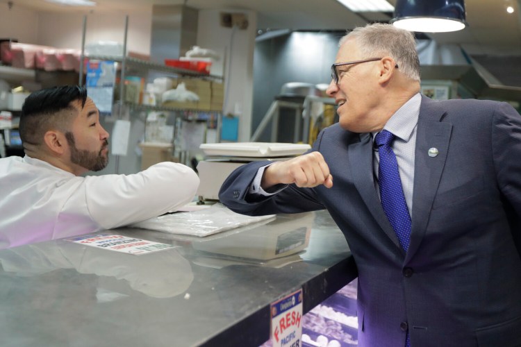 Washington Gov. Jay Inslee, right, bumps elbows with a worker at a Seattle food store.