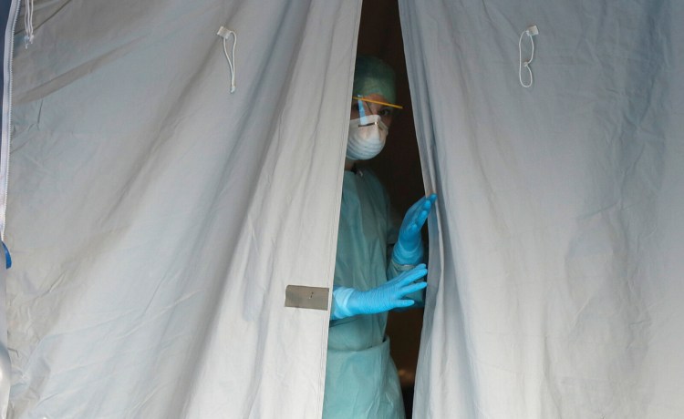 A medical staffer watches from a tent Thursday at one of the emergency structures that were set up to ease procedures at the Brescia hospital in northern Italy. Italians woke up to yet further virus-containment restrictions after Premier Giuseppe Conte ordered restaurants, cafes and retail shops closed after imposing a nationwide lockdown on personal movement. 