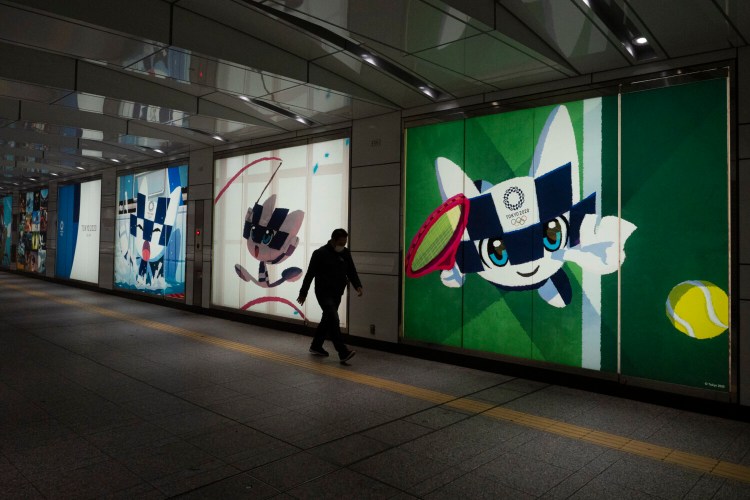 A man walks past large displays promoting the Tokyo 2020 Olympics in Tokyo on Tuesday. IOC President Thomas Bach has agreed "100 percent" to a proposal of postponing the Tokyo Olympics for about one year until 2021 because of the coronavirus outbreak, Japanese Prime Minister Shinzo Abe said Tuesday. 