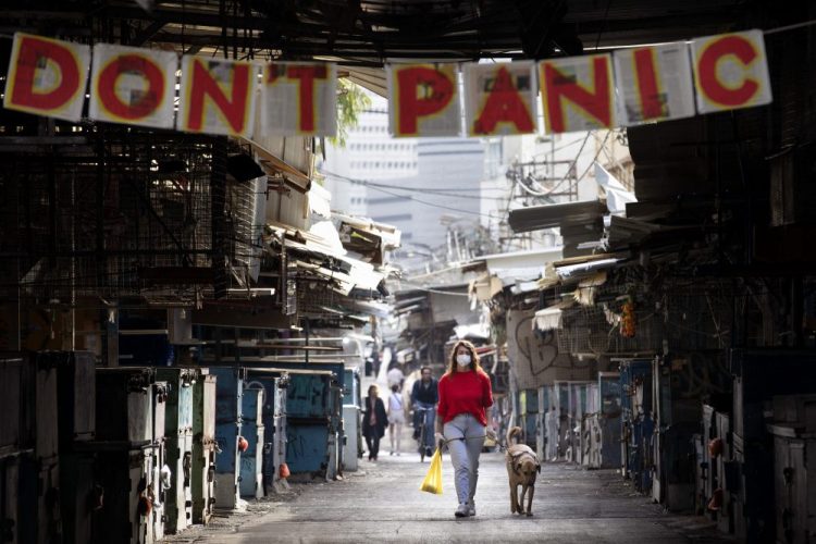 A woman walks her dog under a "don't panic" sign hanging on the entrance of a food market that was shut down Monday in Tel Aviv, Israel.