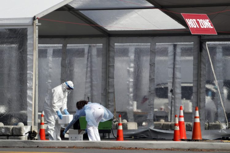 A worker wearing protective gear, left, transfers a container to another worker outside one of the tents at a state-managed coronavirus drive-through testing site that opened Thursday on the Staten Island borough of New York. It is the first such facility in New York City.