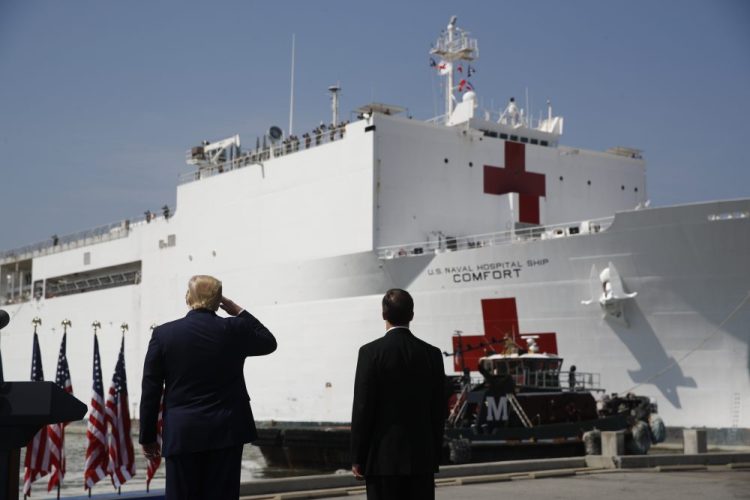 President Trump salutes as the U.S. Navy hospital ship USNS Comfort pulls away from the pier at Naval Station Norfolk in Norfolk, Va., Saturday. The ship is departing for New York to assist hospitals responding to the coronavirus outbreak. Defense Secretary Mark Esper is at right.