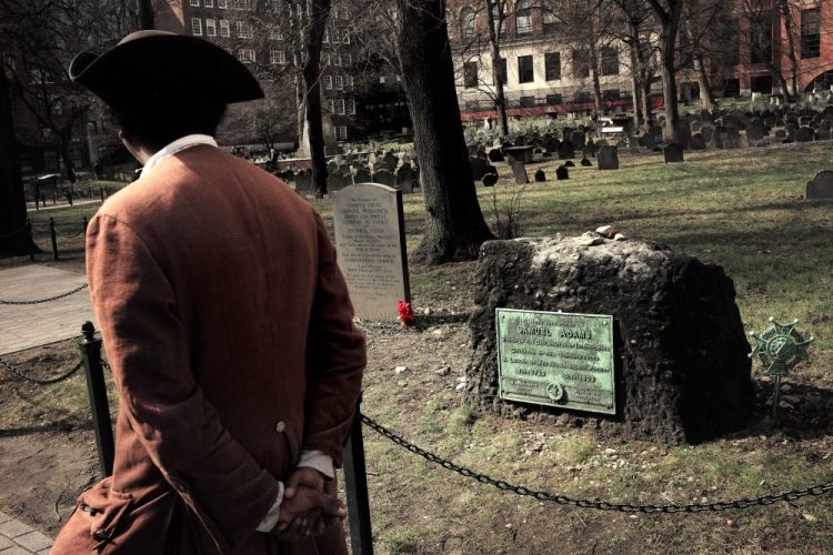 Samuel Ike, of Cambridge, Mass., dressed as Revolutionary War-era African American abolitionist Prince Hall, walks past the grave for victims of the Boston Massacre, left, and for founding father Samuel Adams, right, at the Granary Burying Ground in Boston. On March 5, 1770, British soldiers opened fire on a crowd, klling five people.