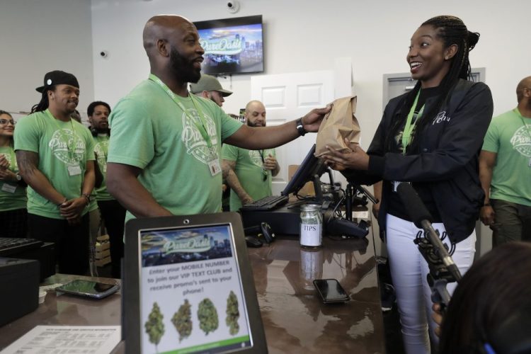 Kevin Hart, front left, co-owner of Pure Oasis recreational marijuana shop, completes a sale of cannabis products to the store's first customer, Niambe McIntosh, moments after the store opened for the first time on Monday in Boston. Pure Oasis is Boston's first recreational marijuana shop.