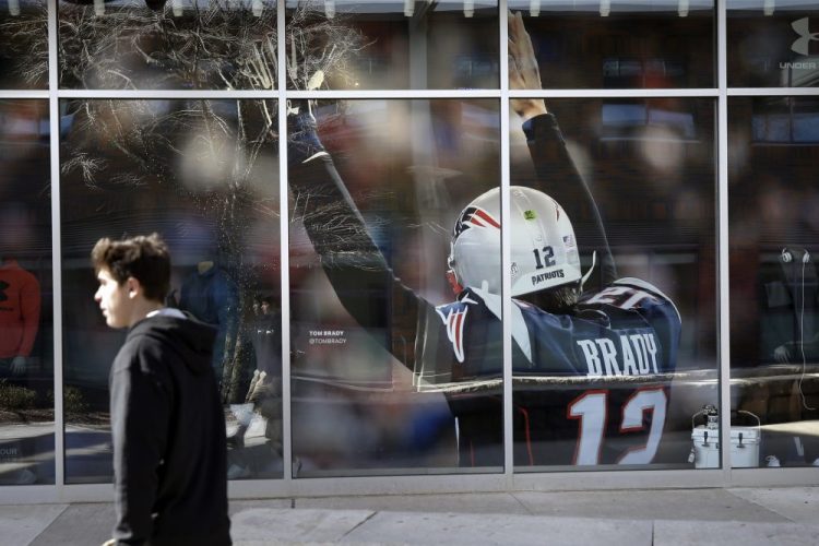 A passer-by walks past an oversized photograph of former New England Patriots football quarterback Tom Brady last week at Patriot Place mall, in Foxborough, Mass. Brady left the Patriots after 20 years and six Super Bowl title last week.